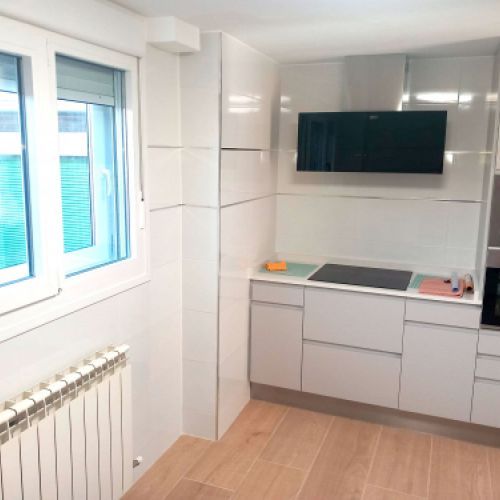 Cocina reformada con muebles blancos y ventana en un lateral