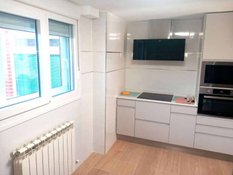 Cocina reformada con muebles blancos y ventana en un lateral